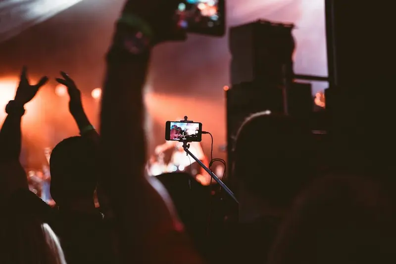 A phone on a pole mount filming the stage over a silhouetted crowd, warm amber