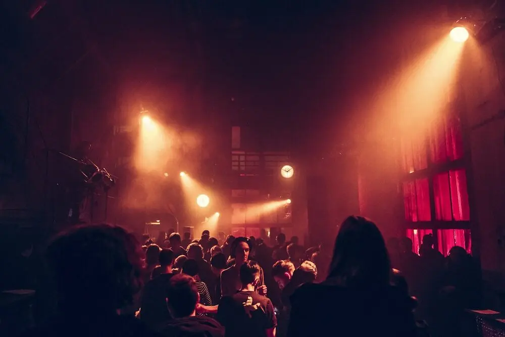 A small venue seen from the back of the crowd, warm stage lights through haze
