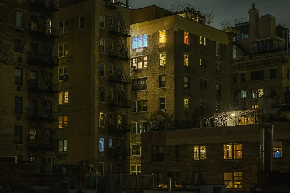Brick walk-ups with fire escapes at night, a few windows lit warm; the photo page places it at East 94th Street & Madison