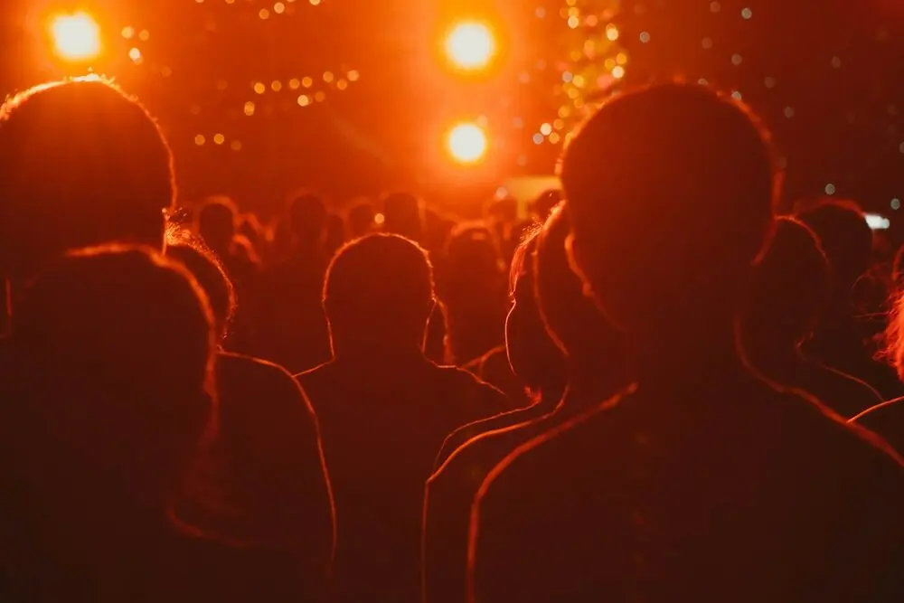 An audience in silhouette from behind, warm orange stage light and haze