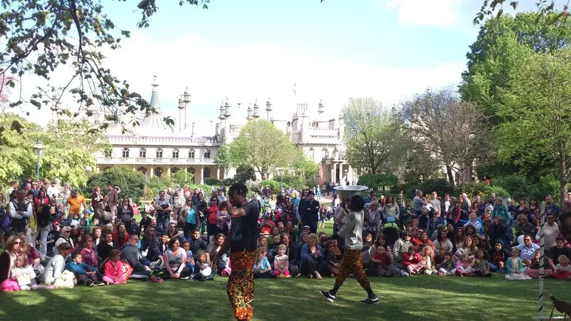 Performers entertaining a large seated crowd on the lawn of Pavilion Gardens during Fringe City, with the Royal Pavilion
