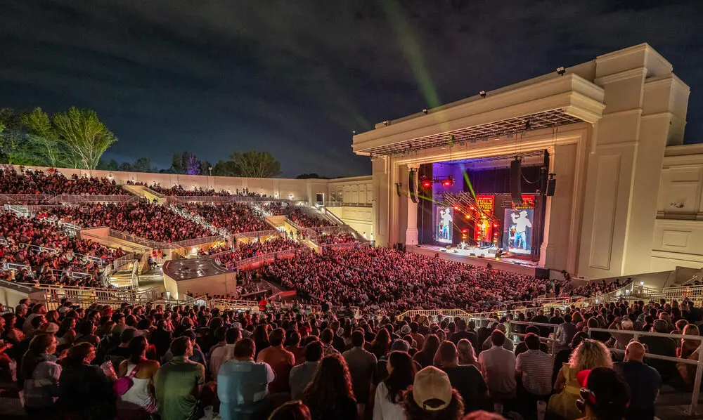 A packed outdoor amphitheatre at night facing the lit Fully Loaded stage and its big screens