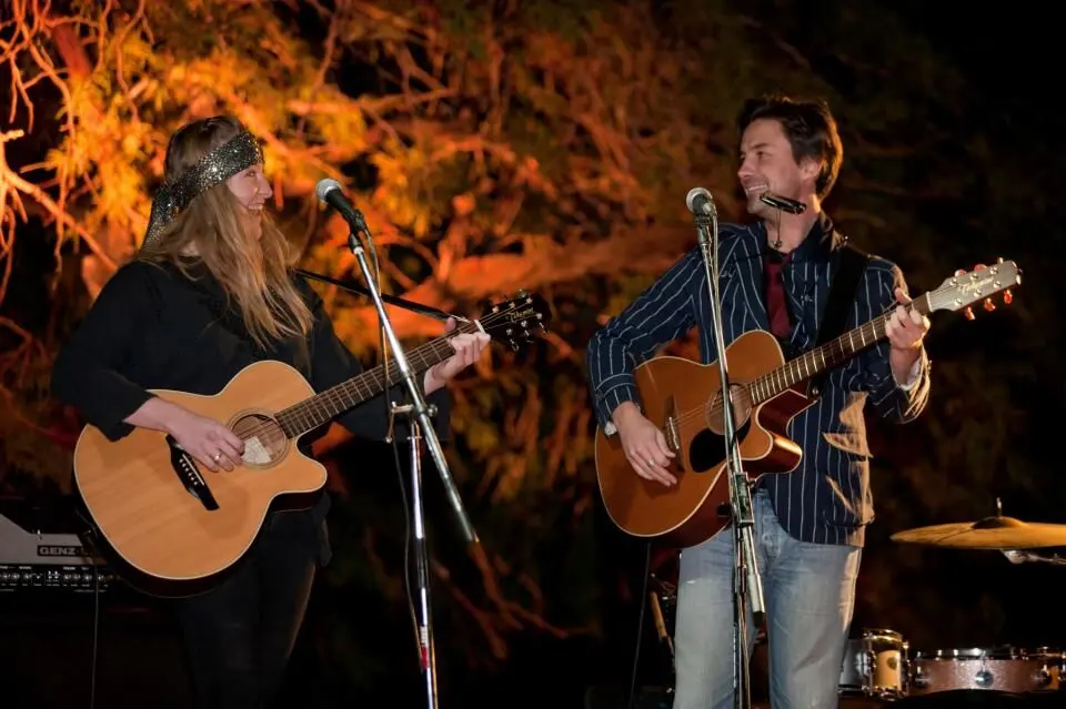 Two musicians playing acoustic guitars on the outdoor stage at The Palms in Wonder Valley, the desert bar that hosts the