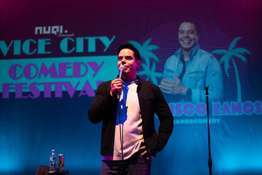 A comedian performing at the mic in front of the glowing Vice City Comedy Festival backdrop