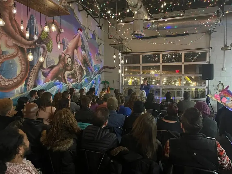 A packed room under string lights and a large octopus mural watching a comedian at the front during the West End Comedy Fest