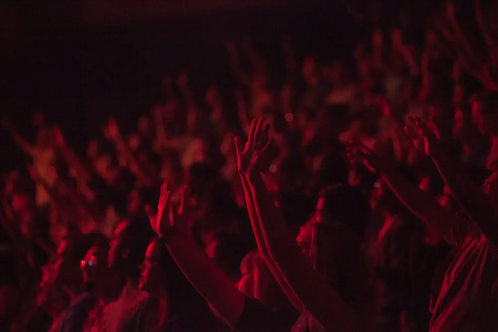 A blurred crowd with hands in the air under deep red stage light