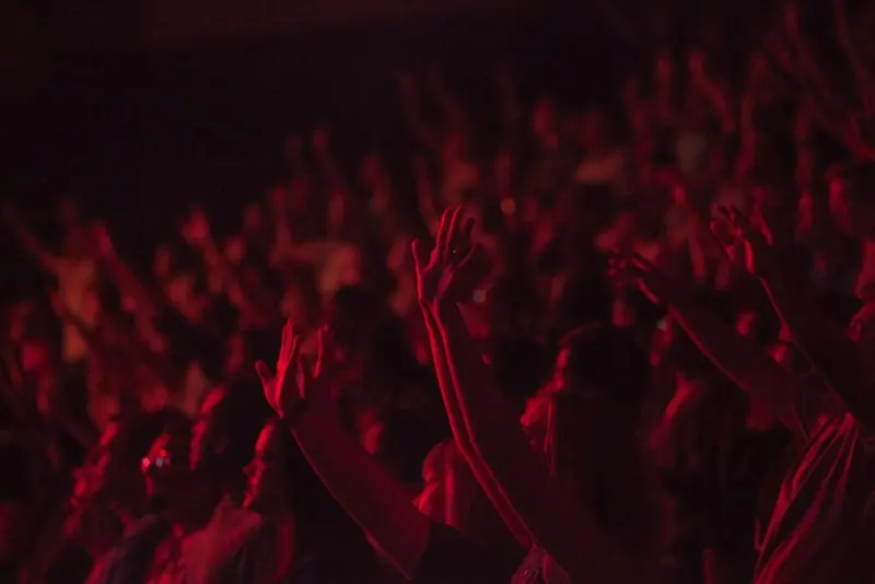 A blurred crowd with hands in the air under deep red stage light