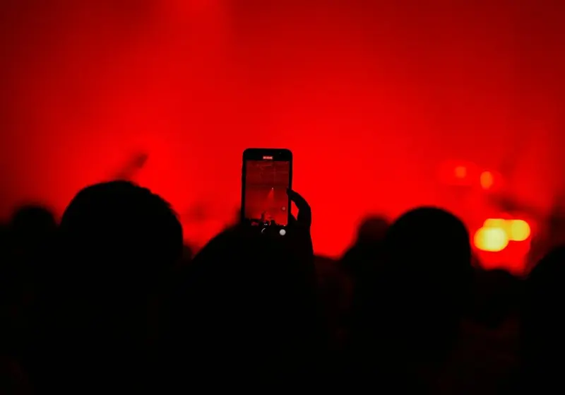 A phone raised over the crowd filming a red-lit stage