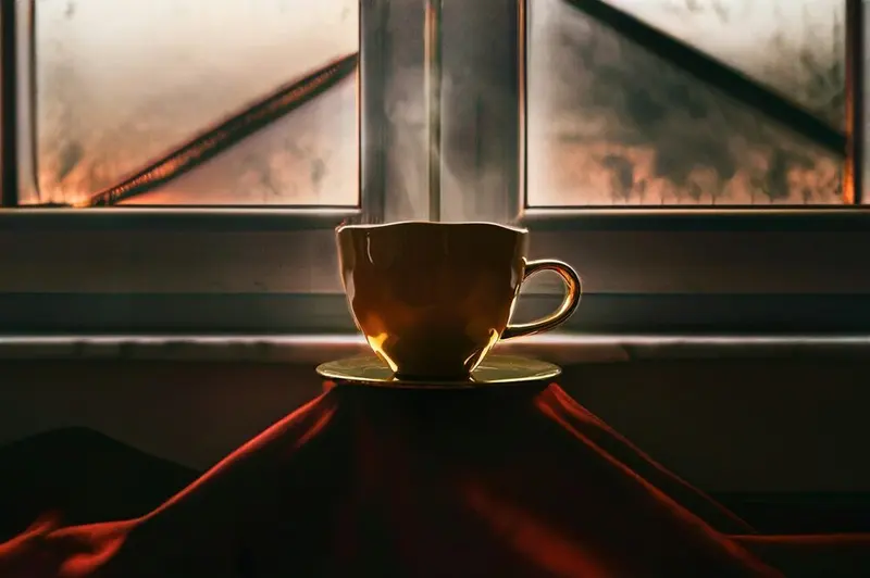 Cup and saucer silhouetted against a misted window at dawn, red cloth below