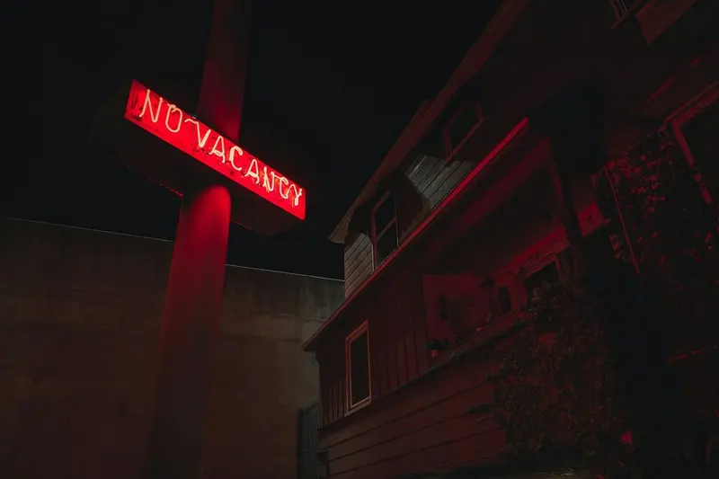 Red neon NO VACANCY sign on a pole beside a motel, night