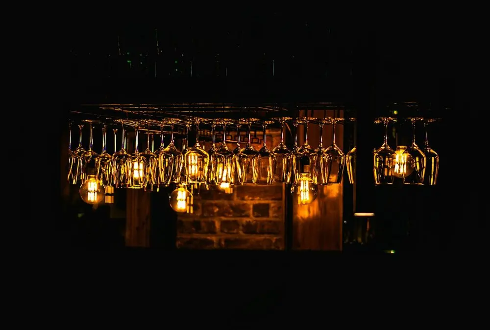 A bar's hanging wine glasses and filament bulbs glowing over dark brick, lights just on